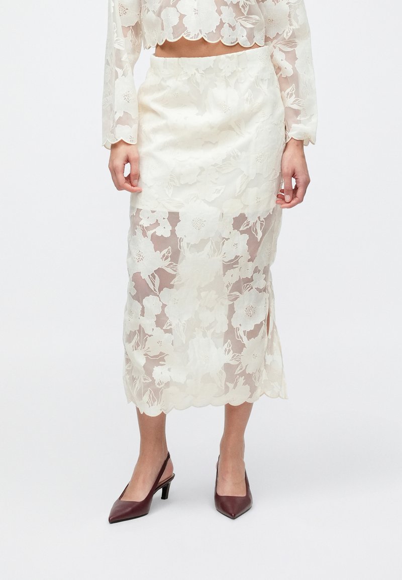 Doorzichtige bloemenkant rok in off-white met een geschulpte zoom en een aansluitend silhouet, gecombineerd met bordeauxrode pumps met puntige neus.