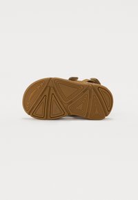 Brun sandal med en texturerad gummisula med geometriskt mönster; justerbar remdesign för säker passform.