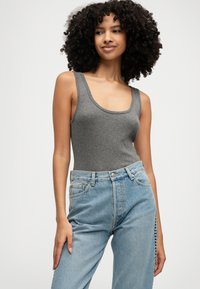 Top en tank gris sans manches avec un décolleté arrondi, associé à un jean en denim bleu clair taille haute avec un détail latéral discret.