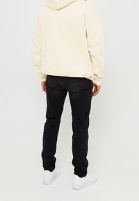 Witte hoodie met een losse pasvorm, gecombineerd met zwarte slim-fit jeans en witte sneakers. De stof lijkt zacht te zijn met geribbelde manchetten.