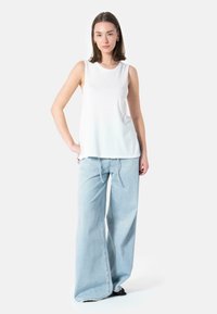 Hvit ermeløs topp med rund hals sammen med lyseblå vide jeans med snøring i livet. Enkel, uformell design.
