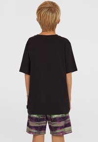 Svart kortermet t-skjorte med rund hals, sammen med flerfargede shorts med stripete mønster i grønn, lilla og svart.