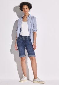 Szorty dżinsowe z podwiniętymi mankietami, zestawione z białą koszulką na ramiączkach i niebiesko-białą koszulą zapinaną na guziki, w luźnym kroju oraz casualowymi trampkami.