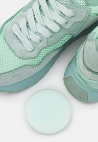 Miętowo-zielone sneakersy wykonane z siateczki i zamszu, z okrągłym wkładką z pianki w dopasowanym kolorze, prezentujące sznurowadła i teksturowane akcenty.