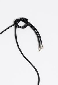 Czarny skórzany sznurek skręcony w węzeł z dwoma srebrnymi metalowymi końcówkami na końcu. Gładka tekstura i elegancki design, na białym tle.