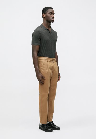 Short-sleeve dark gray polo, khaki trousers, and black sneakers. Pants have a straight leg, subtle texture, and classic design details.