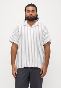 Πουκάμισο με κοντά μανίκια σε λευκό χρώμα με γκρι ρίγες, διαθέτει κουμπιά στο μπροστινό μέρος και άνετη γραμμή. Το ύφασμα φαίνεται ελαφρύ με ελαφρώς υφή ύφανσης.