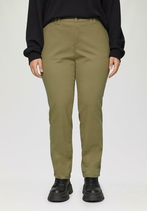 Olijfgroene broek met een rechte pasvorm, zijzakken en riemlussen, gedragen met zwarte schoenen met dikke zolen en een zwarte gestructureerde top.