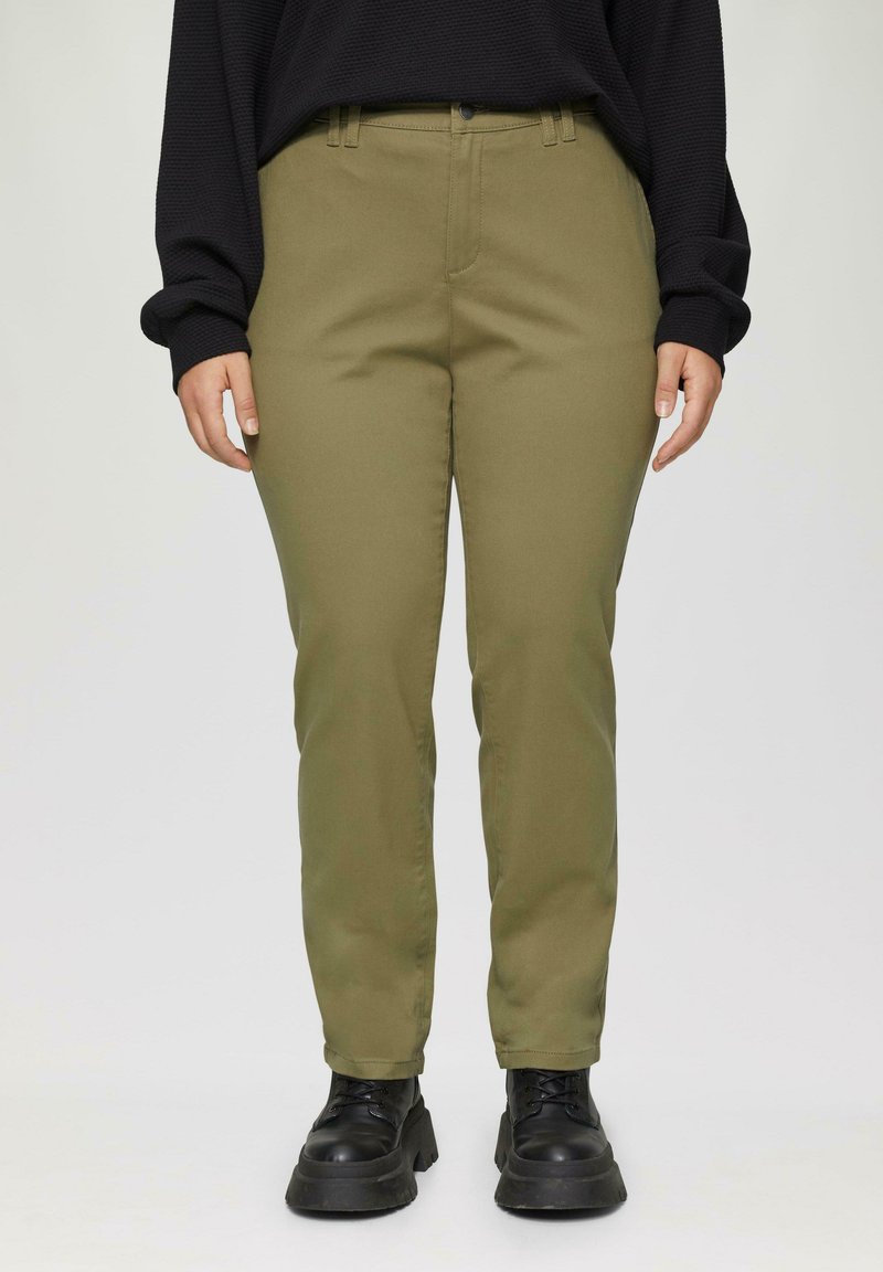 Olijfgroene broek met een rechte pasvorm, zijzakken en riemlussen, gedragen met zwarte schoenen met dikke zolen en een zwarte gestructureerde top.