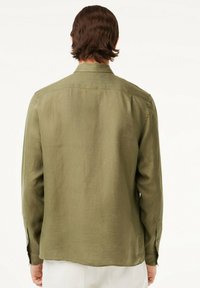 Camicia a maniche lunghe verde oliva in lino. Presenta un taglio dritto, polsini con bottoni e un design posteriore pulito senza dettagli visibili.