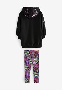 Schwarze Kapuzenjacke mit Spritzmuster in Pink und Blau auf der Kapuze; kombiniert mit bunten Leggings, die floral und abstrakte Designs zeigen.