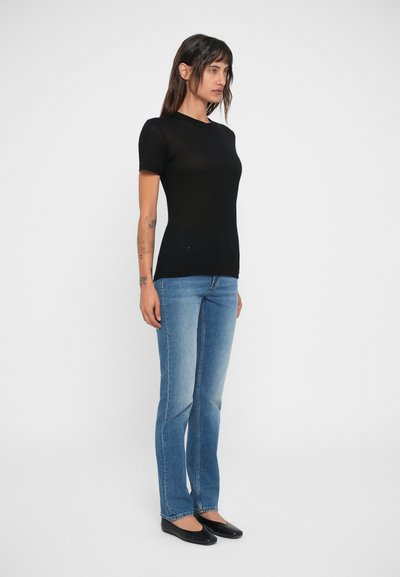 Tricou negru slim fit cu mâneci scurte, asociat cu blugi drepți de un albastru deschis și pantofi negri fără toc. Design minimalist, textură fină.