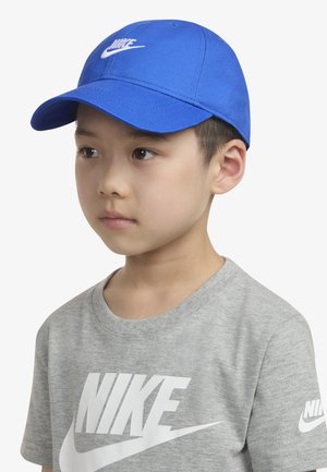 Sinine Nike nokamüts kaareva visiiri ja tikitud logoga. Hall Nike t-särk, millel on suur valge logotekst. Puhas disain ja pehme tekstuur.