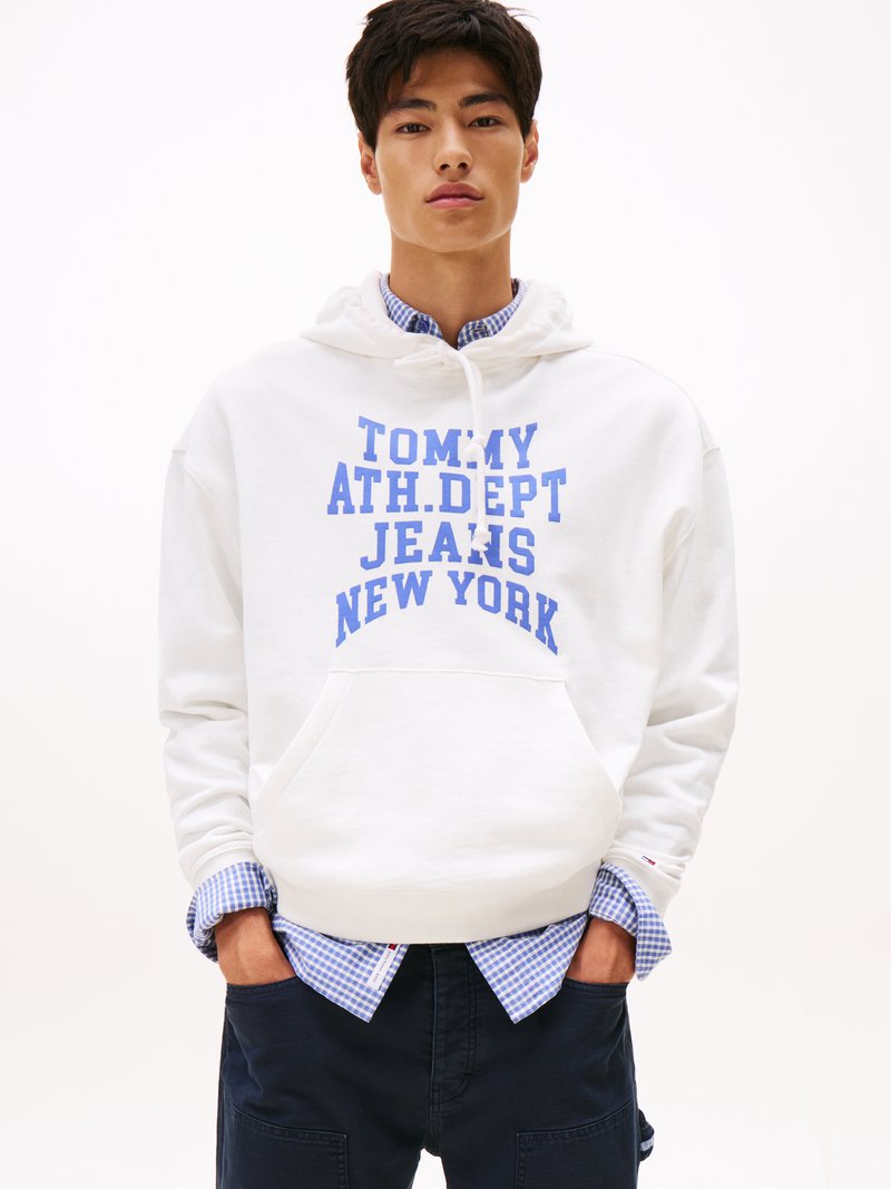 Weißer Hoodie mit blauer Schrift, die "TOMMY ATH. DEPT JEANS NEW YORK" liest, übereinander getragen mit einem blau karierten Hemd und dunklen Hosen. Einfaches Design.