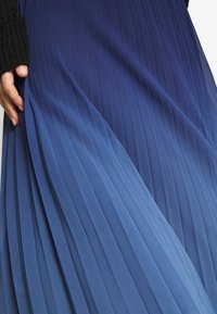 Fållad kjol i en gradient från mörk till ljusblå. Gjord av ett mjukt tyg med vertikala ribbor, med en mjuk textur och ett flödande design.