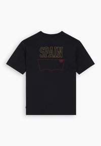 T-shirt en coton noir à manches courtes, avec "ESPAGNE" écrit en jaune et un contour de poche en jean rouge au dos.