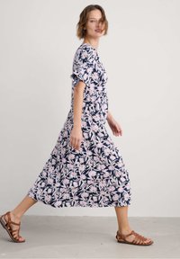 Floral maxi dress with short sleeves, navy background, pink and white flower pattern, loose fit, paired with brown strappy sandals.