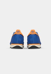 Blue suede athletic shoes with orange accents and white soles. Features include rounded heel and a logo at the back. Smooth texture overall.