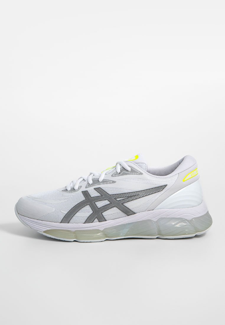 Zapatilla de correr gris claro y blanca con rayas negras, suela de gel y detalles amarillos, vista desde el lado exterior sobre un fondo blanco.