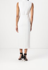 Robe midi blanche sans manches avec corsage ajusté, taille élastique, texture lisse et détail zippé. Associée à des talons noirs avec brides à la cheville.