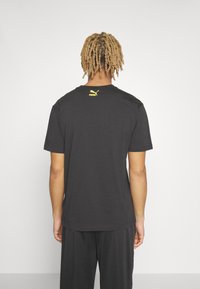 Sort bomulds t-shirt med rund hals, korte ærmer og et lille gult Puma-logo på den øverste ryg. Glat tekstur, afslappet pasform.