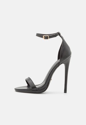 Czarne sandały na wysokim obcasie z cienkim paskiem wokół kostki i pojedynczym paskiem na palce. Posiadają spiczasty kształt palców i błyszczące wykończenie. Złota klamra jako dodatek.