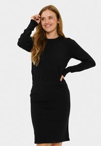 Robe noire à manches longues en tissu doux, silhouette ajustée avec une couture à la taille, détails côtelés aux manches et à l'ourlet, longueur genou.