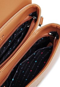 Hnědá kožená taška s třemi zipovými přihrádkami a podšívkou se vzorem puntíků v modré, červené a bílé barvě na tmavém pozadí.