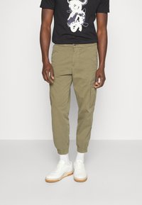 Karakipade tapered cargobyxor med elastiska muddar, sidofickor och knappstängning fram, tillsammans med en svart grafisk t-shirt och vita sneakers.
