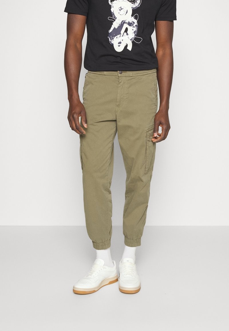 Karakipade tapered cargobyxor med elastiska muddar, sidofickor och knappstängning fram, tillsammans med en svart grafisk t-shirt och vita sneakers.