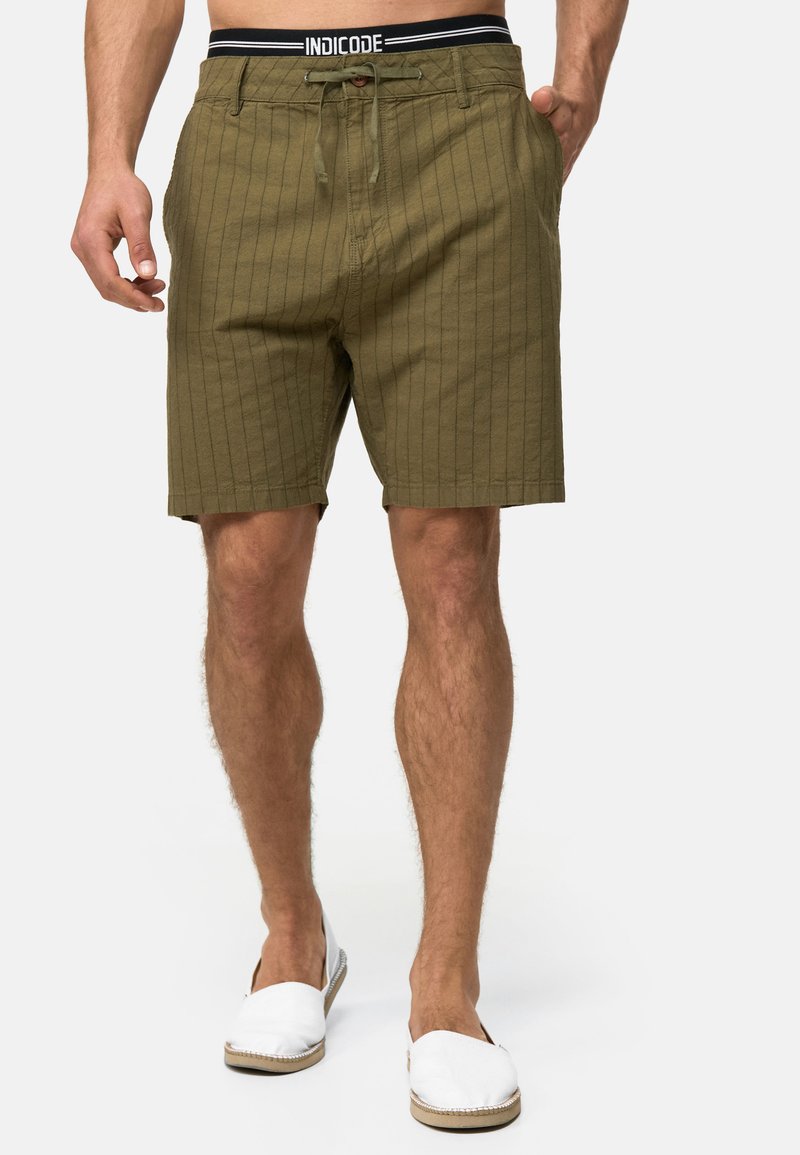 Olivengrønne shorts med lodrette striber, en snoreliv og forlommer. Båret med hvide slip-on sko.