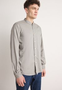 Lys grå langermet skjorte med en bandkrage, med knappestolpe foran og lett gathered ermer. Båret med mørkeblå jeans.