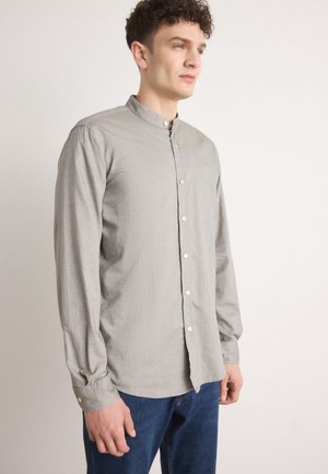 Lichtgrijs langslijfshirt met een bandkraag, voorzien van een knoopsluiting aan de voorkant en lichtjes gerimpelde mouwen. Draagt met donkerblauwe jeans.
