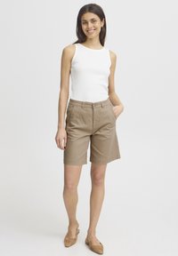 Shorts en coton beige avec une taille élastique, poches avant et coupe décontractée, associés à un débardeur blanc à côtes et des ballerines beiges.