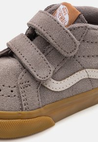 Zapatilla de ante gris con dos correas de Velcro, acento de cuero blanco y suela de goma. Presenta costuras reforzadas y perforaciones.