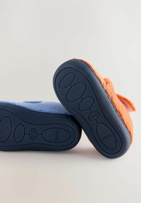 Deux paires de chaussons doux et en peluche, en bleu clair et en orange, avec des semelles en caoutchouc noir, présentant un motif de grip texturé et une forme arrondie.