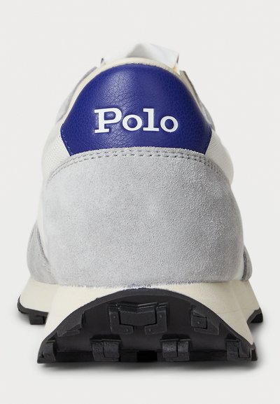 Grey suede and white sneaker heel with black rubber sole and blue leather patch displaying "Polo" branding in white text.