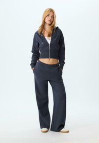 Felpa corta navy con zip, orlo a costine, abbinata a pantaloni della tuta navy a vestibilità ampia con vita elasticizzata e tasche laterali.