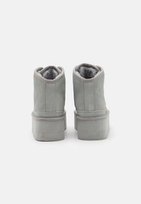 Bottines en suede gris avec une doublure intérieure douce, des semelles en caoutchouc plates et des accents cousus le long des coutures et du col.