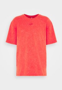 Červené tričko s krátkým rukávem vyrobené z bavlny s vybledlým vzhledem. Na hrudi má malé vyšité logo Nike. Design s kulatým výstřihem.