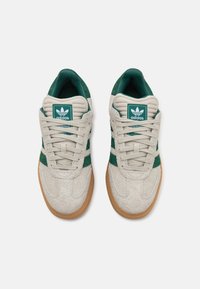 Un paio di sneakers Adidas in suede beige e verde con suole in gomma, vista dall'alto, allacciate e con il logo Adidas sulla linguetta.