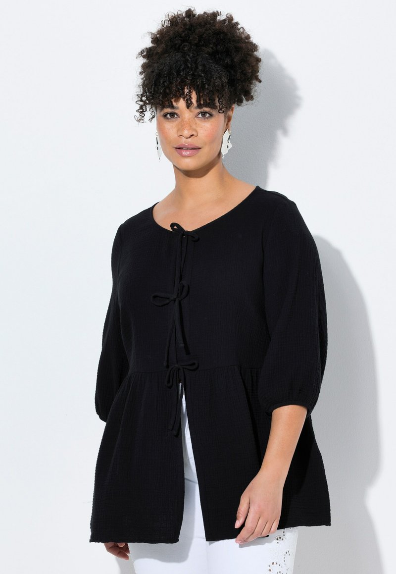 Black, textured top with a round neckline, puffed sleeves, and front tie detail. The design features a peplum silhouette for added fullness.