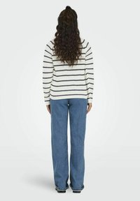 Knitted sweater with white and navy stripes, paired with loose blue jeans. The sweater features a textured pattern and a rounded hem.