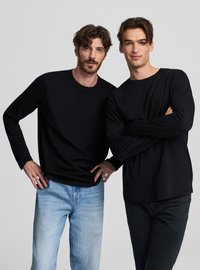 Due uomini che indossano maglie nere a maniche lunghe. Uno ha jeans blu, l'altro pantaloni neri. Le maglie hanno un semplice design con girocollo.