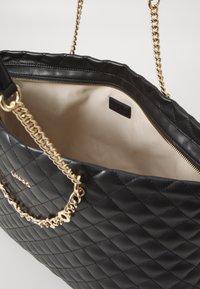 Sac à main en simili cuir noir matelassé avec une chaîne dorée, doté d'une fermeture éclair et d'une doublure intérieure beige avec une étiquette de marque à l'intérieur.