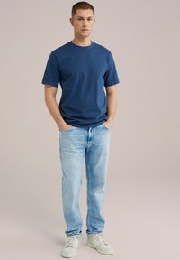 T-shirt in cotone blu navy con maniche corte, abbinato a jeans in denim chiaro. L'outfit è completato con sneakers bianche da ginnastica.