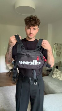 Bolsa crossbody preta com alças ajustáveis, fecho com zip e acabamentos vermelhos. Apresenta um logo branco proeminente "ellesse" na frente.