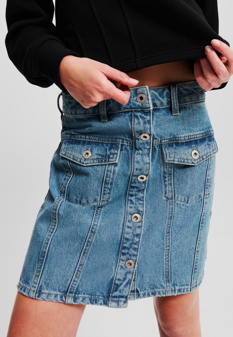 Denim krilo v svetlo modri barvi, z sprednjim gumbnim zapiranjem, dvema žepoma na prsih in oprijetim krojem. Ožigosana tekstura na robu.