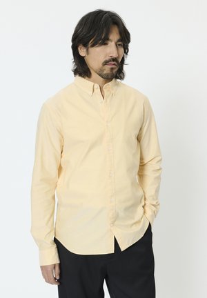 Jasnożółta koszula na guziki, wykonana z bawełny, z długimi rękawami. Posiada klasyczny kołnierz, plisę z przodu oraz zaokrąglony dół.