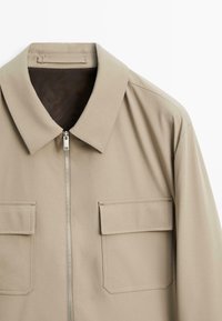 Beige zip-up jack met een klassieke kraag, twee borstzakken, een soepele textuur en nauwkeurige stiksels. Voorzien van een duurzame rits en een minimalistisch ontwerp.